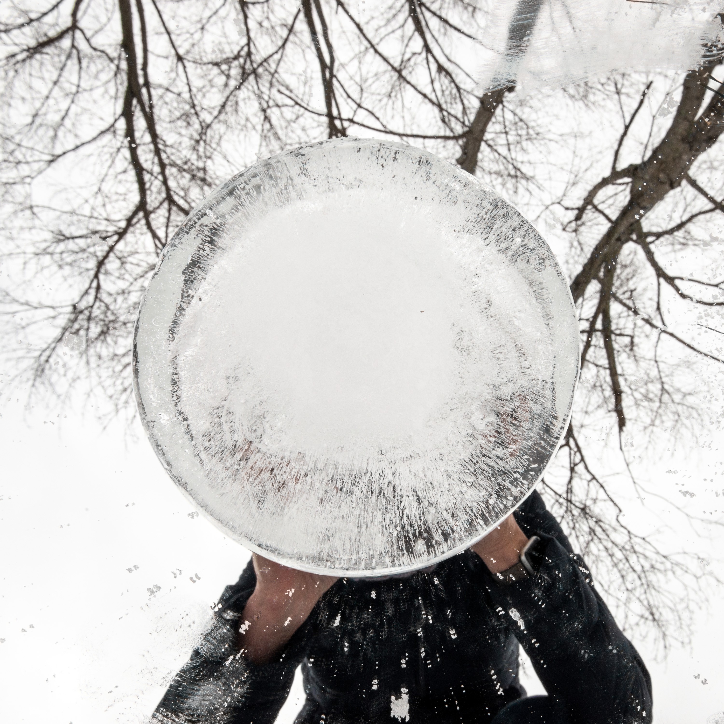 Person holding a sphere of ice blocking their face. 