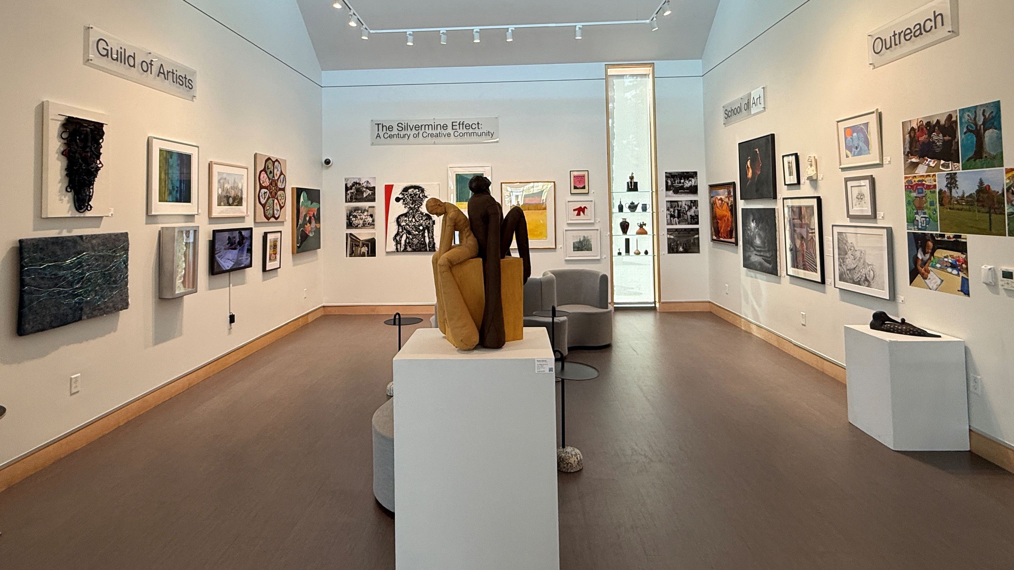 View of gallery from the front with sculpture in center and work hung on three sides