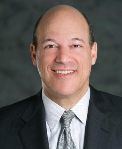 Bald man with white shirt, tie, and dark suit smiling at camera
