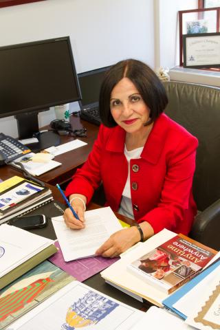 White woman with black bobbed hair seated at desk writing with a pen
