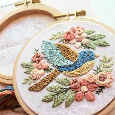 This image shows an embroidery sampler with a blue bird and ring of flowers.