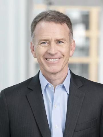 White man with closely cropped brown hair wearing a light blue shirt and dark blazer smiling directly at camera