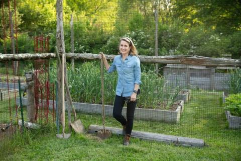 Photo of a white woman with blonde hair standing in front of garden fencing. 