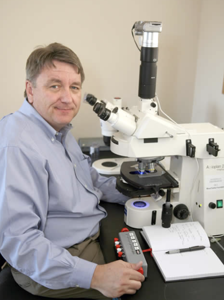 Man turning away from large microscope to face viewer