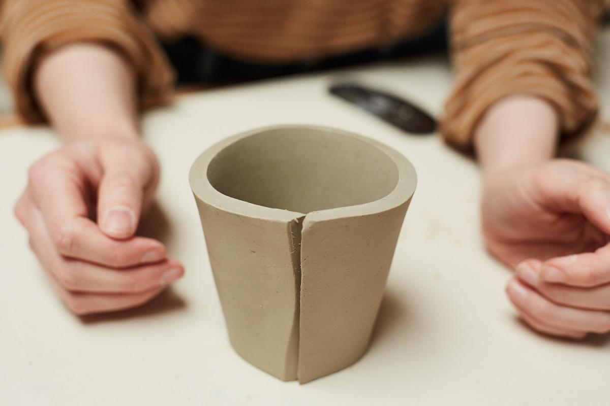 Hands on either side of a partially built clay mug