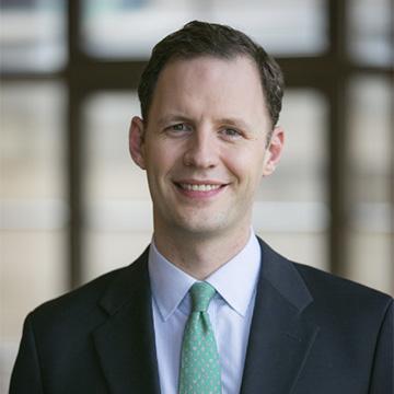 White man with short haircut wearing white shirt, green tie, navy blazer and smiling at camera