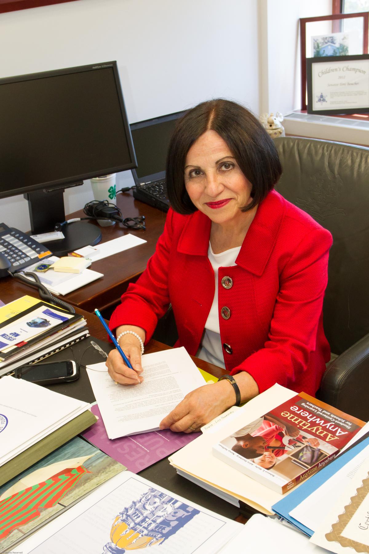 White woman with black bobbed hair seated at desk writing with a pen