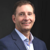 Photo of white man with brown hair in a light blue collared shirt and navy blazer