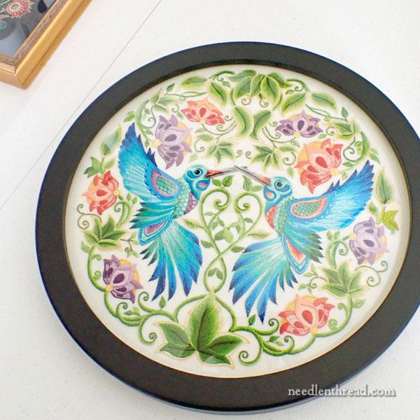 Two embroidered blue hummingbirds face each other. There is delicate filigree surrounding them.